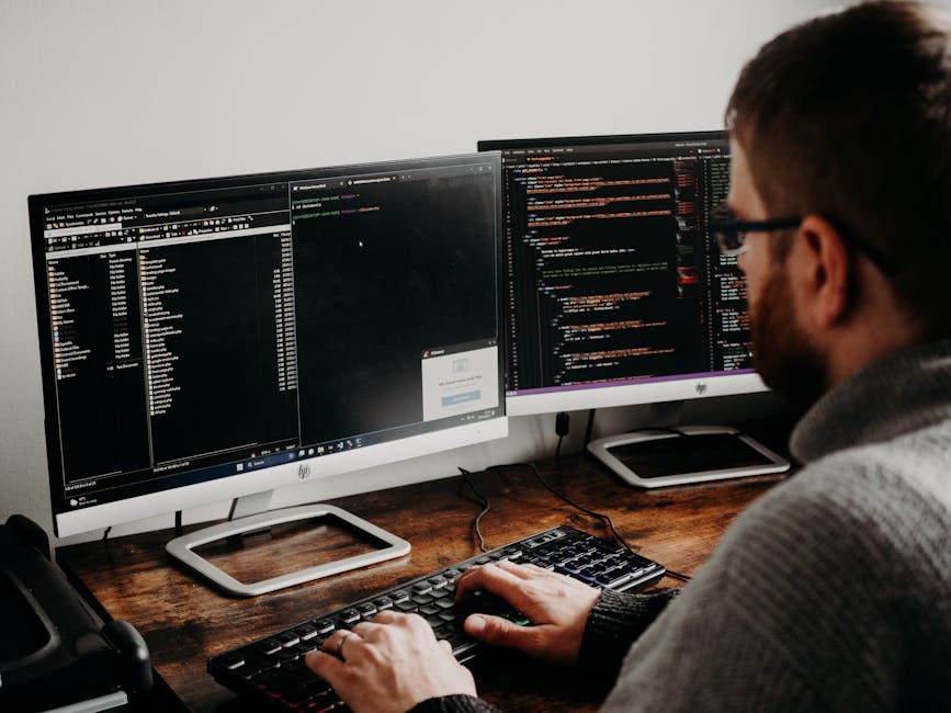 The image features a person wearing a long-sleeved, white and navy striped shirt operating a silver laptop placed on a white kitchen countertop. The laptop's screen displays lines of colored code on a